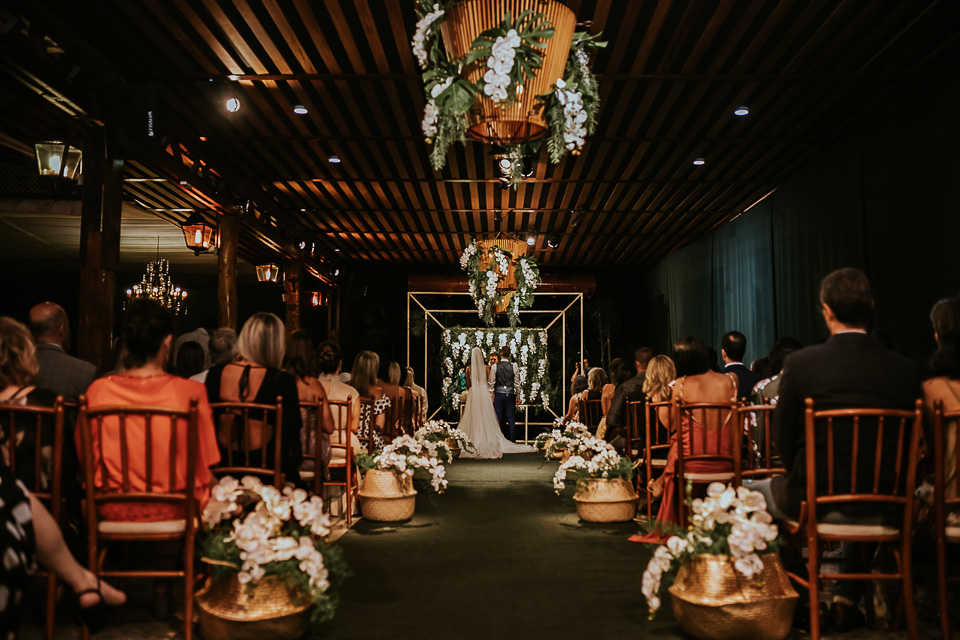 Convidados sentados em cadeiras de madeira marrom, noivos sendo casados.
