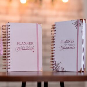 dois planners de casamento o da esquerda com capa rosa e o da direita com capa branca e flores nos cantos inferior esquerdo e superior direito